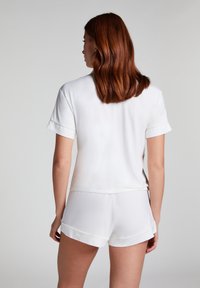 Haut blanc à manches courtes en tissu lisse avec des poignets roulés, associé à un short blanc assorti avec un design de revers plié.
