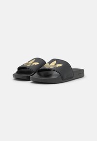 Svarta slidesandaler med en texturerad sula och bred rem som har en guldlogo. Tillverkade av syntetiskt material, designade för vardagsbruk.
