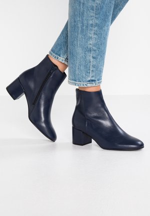 Bottines en cuir bleu marine avec talons carrés et fermetures éclair latérales, portées avec un jean denim bleu clair.