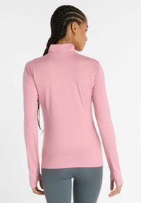 Langarmshirt aus hellrosa Stoff mit einem Stehkragen. Glatte Textur, taillierte Passform, mit verlängerten Bündchen.