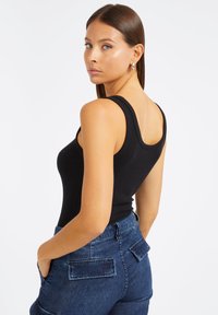 Débardeur noir côtelé avec un dos échancré. Porté avec un pantalon en denim bleu foncé taille haute avec de grandes poches arrière.