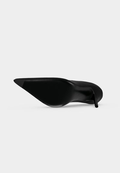 Chaussure noire à talon stiletto pointu, couchée sur le côté, montrant la semelle et le talon fin sur fond uni.