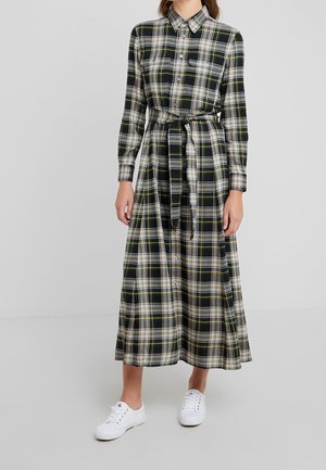 Sukienka w kratę w kolorach czarnym, białym i żółtym, z długim rękawem, guzikami, wiązaniem w talii i dwoma kieszeniami na piersiach; zestawiona z białymi trampkami.