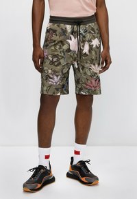 Shorts camouflage vert olive avec un motif floral en rose et violet, dotés d'une taille élastique et d'un cordon de serrage.