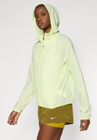 Ελαφρύ μπουφάν με κουκούλα σε έντονο κίτρινο χρώμα. Διαθέτει φερμουάρ στο μπροστινό μέρος και ένα μικρό λογότυπο. Το ύφασμα φαίνεται λείο και ελαφρώς γυαλιστερό.