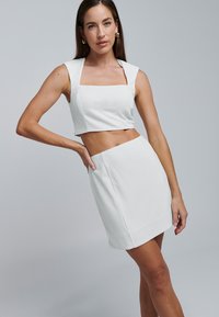 Bela dvodelna obleka s krilcem s štirimi širokimi naramnicami in usklajeno mini krilo. Tkanina s teksturo vsebuje subtilne detajle.