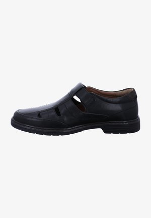 Black leather shoe with open cutouts, flat sole, and a Velcro strap. Features smooth texture and stitching accents. Designed for comfort and breathability.