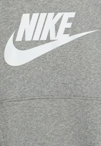 Šedá mikina vyrobená z měkké tkaniny s velkým bílým logem "NIKE" a designem swoosh. Textura vypadá hladce s mírným leskem.