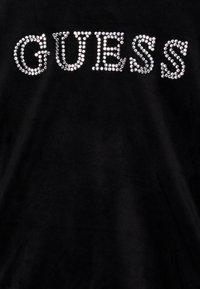 T-shirt in tessuto nero con la parola "GUESS" in strass argento. Collo rotondo semplice e texture morbida.