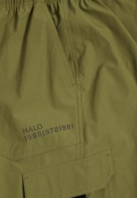 Olivgrüne Shorts aus leichtem Stoff, mit großer seitlicher Tasche, elastischem Bund und geprägtem Text "HALO 196819721981".