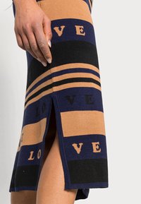 Robe tricotée arborant des rayures horizontales en bleu marine, beige et noir avec le texte "LOVE". Détail fendu sur le côté pour plus de mobilité. Texture lisse.
