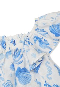Top in tessuto bianco con motivi a conchiglia blu e marini, caratterizzato da un colletto arricciato e maniche a volant per un tocco di texture e dettaglio.