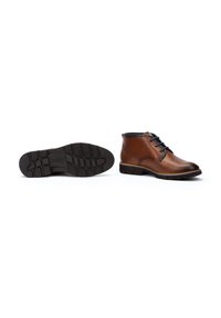Botas de tobillo de cuero marrón con cordones negros, punta redondeada y suela de goma con un patrón de relieve. Incluye un detalle de costura en contraste.