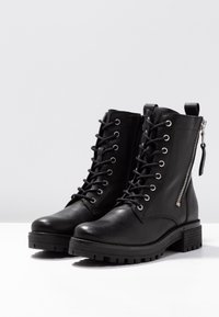 Bottes cheville en cuir noir avec fermeture à lacets sur le devant, fermeture éclair latérale, semelle épaisse et finition texturée. Comprend une languette de tirage à l'arrière.