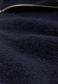 Mörk marinblått tyg med en mjuk, fluffig textur och en suddig guldkedja som löper horisontellt nära toppen.