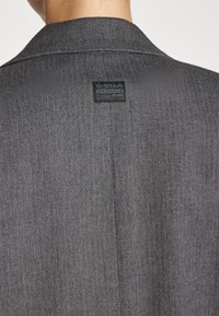 Szary żakiet w jodełkę z delikatnym połyskiem, ostrymi klapami i czarną metką G-Star Originals przy kołnierzu.