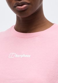 Κοντινό πλάνο ενός ατόμου που φοράει ροζ πουκάμισο με το λογότυπο της Berghaus σε λευκό, το οποίο είναι τοποθετημένο στο κέντρο του στήθους.