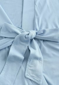 Vaalean sininen kangas, jolla on sileä pinta, keskellä on solmittu vyö ja päällekkäin asettuvia paneeleita. Ompeleet näkyvät reunoissa.