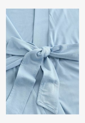 Svetlo modra tkanina z gladko teksturo, ki ima v središču zavezano trako in prekrivajoč dizajn panelov. Vidni so šivi.