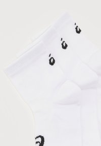 Τρία ζεύγη λευκές κάλτσες για άντρες με μαύρο μικρό γράμμα "á" κοντά στη μανσέτα, στοιβαγμένα διαγώνια σε λευκό φόντο.