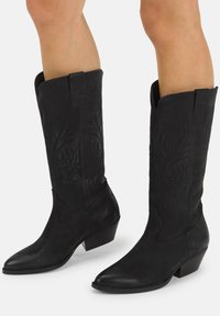 Botas de vaquero de cuero negro con intrincados bordados tonales, punta afilada, tacón medio en bloque y patrones decorativos en relieve en el cañón.