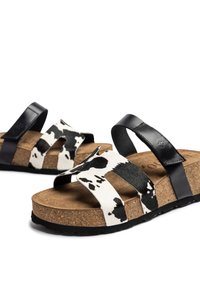 Black and white cow-print slide sandals with two straps, cork footbed, and a textured black rubber sole. Soft animal-friendly material.