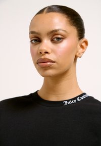 Must t-särk ümmarguse kaelusega ja valgete "Juicy Couture" tähtedega krae peal. Sile kangas, lihtne disain, keha järgnev lõige.