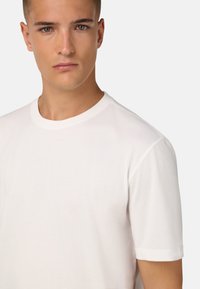 Valge crew-neck t-särk, mis on valmistatud puuvillast, lühikeste varrukatega ja lihtsa, siledaga tekstuuriga. Pole nähtavaid mustreid ega aktsente.