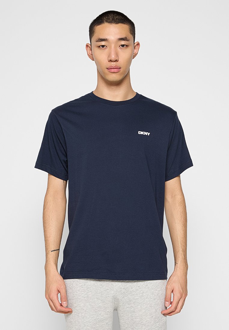 Granatowa bawełniana koszulka z krótkim rękawem, żebrowanym okrągłym dekoltem i białym logo DKNY na lewej piersi. Luźny krój, gładka struktura.
