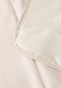 Ljus beige tyg med en slät textur, som har en sydd kant och en subtil glans. Designen inkluderar en förstärkt kant.