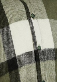 Gros plan sur un tissu à carreaux vert, noir et blanc avec une couture verticale à boutons comportant de petits boutons vert foncé.