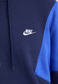 Kék és tengerészkék kapucnis pulóver, pamutból készült, fehér Nike logóval, zsinóros kapucnival, színblokkolt mintával.