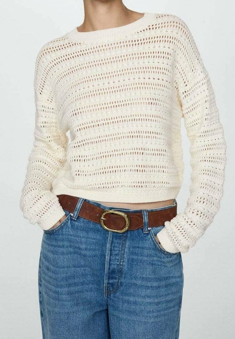 Pull tricoté couleur crème avec une coupe ample, présentant une texture à trame ouverte. Assorti à un jean en denim bleu taille haute et une ceinture marron.