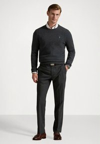 Siva pletena majica z okroglo izrezom, kombinirana z elegantnimi temno sivimi hlačami in rjavimi usnjenimi čevlji. Diskretna podrobnost logotipa na majici.