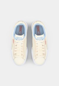 Beige Sneaker mit strukturiertem Obermaterial, blauen Einlegesohlen, weißen Gummisohlen und rotem Markenlogo an den Seiten und auf der Zunge.