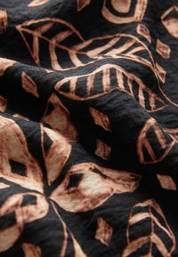 Tissu noir texturé arborant un motif complexe de feuilles marron clair et de formes en losange, créant un contraste audacieux dans le design.