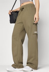 Calças cargo verde oliva fabricadas em material suave, com cintura elástica ajustável e bolso lateral, acompanhadas de sapatilhas brancas.