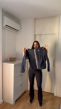 Femme debout dans une pièce tenant une veste bleu marine avec une bande verticale jaune et blanche sur le devant.