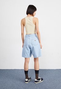 Shorts en denim bleu clair avec une coupe ample, une taille haute et deux poches arrière. Assortis à un haut sans manches beige et des baskets noires.