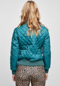 Teal, vadderad bomberjacka med ribbade muddar och nederkant. Har en figursydd design och strukturerad yta. Kapslad med leopardmönstrade leggings.