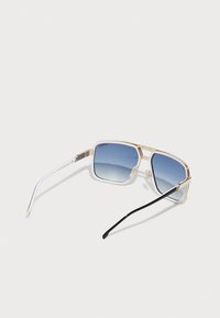 Ochelari de soare cu ramă metalică aurie și ochelari cu gradient albastru. Brațe groase din acetat alb și negru, cu accente metalice. Formă pătrată.