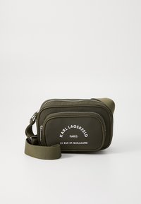 Borsa a tracolla verde oliva realizzata in materiale testurizzato, con doppio scomparto con zip e logo stampato bianco sul davanti. Cinghia regolabile.