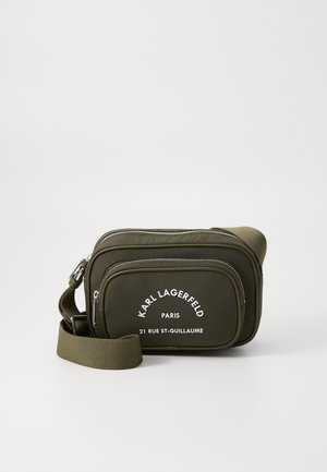 Sac bandoulière vert olive en matériau texturé, doté de deux compartiments zippés et d'une marque imprimée en blanc à l'avant. Bandoulière réglable.