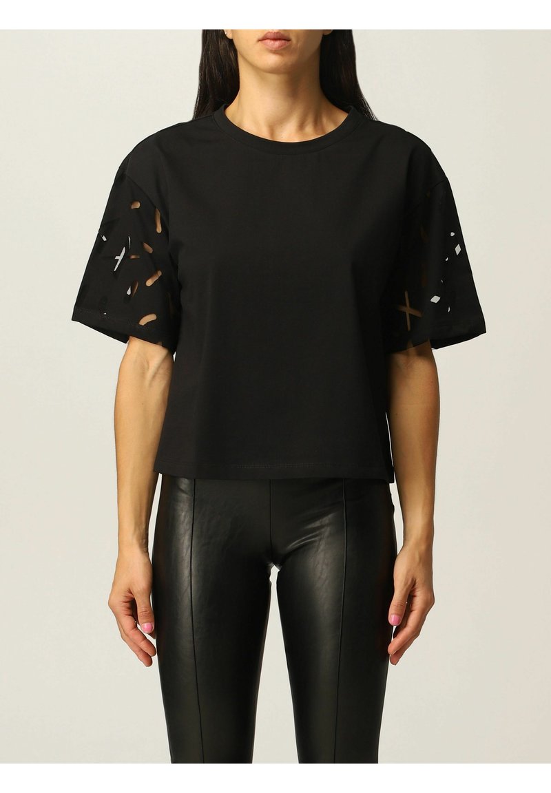 T-shirt noir à manches courtes avec des découpes sur les manches, fabriqué en tissu doux, associé à des leggings noirs en simili cuir ajustés.