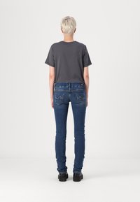 Camiseta de algodón gris de manga corta, combinada con jeans ajustados de mezclilla azul con bolsillos traseros y acentos desvanecidos. Zapatos de plataforma negros.