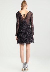 Schwarzes Blumenmusterkleid mit transparenten langen Ärmeln, einem V-förmigen Rückenausschnitt und einer Bindung. Verfügt über einen ausgestellten Rock und wird mit glänzenden silbernen Stiefeletten getragen.