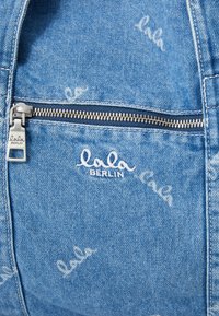 Μπλε τζην τσάντα με ασημί φερμουάρ, που διαθέτει λευκό κεντημένο λογότυπο "lala" και διακριτικό ολοκληρωμένο σχέδιο με το όνομα της μάρκας.