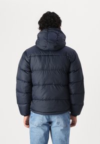 Giacca puffer blu navy con cappuccio, con un design trapuntato e polsini elasticizzati. Tessuto caldo e leggero per l'isolamento.