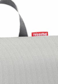 Grau gewebte Tragetasche im Chevron-Muster, mit einem schwarz-weißen gestreiften Griff und einem roten "reisenthel"-Label.