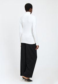 Pull en col roulé blanc avec des manches longues, design ajusté et ourlet côtelé, assorti à un pantalon large noir et des mules à talons hauts noir.